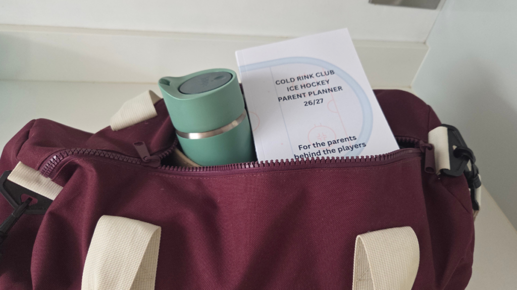 Image of a maroon coloured bag, partially zipped, with a green travel flask and Cold Rink Club Ice Hockey parent planner peaking through